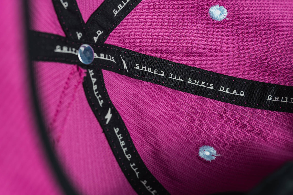 Close-up of the Shred Til She's Dead Corduroy 5-Panel Hat's pink interior, showing black stitching, branded labels, small blue rivets, a shiny button, and a moisture-wicking sweatband.