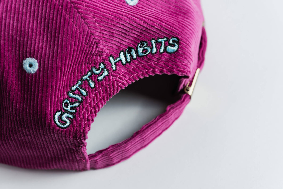 Close-up of the back of the “Shred Til She's Dead” pink corduroy 5-panel hat with light blue “GRITTY HABITS” embroidery, moisture-wicking sweatband, and metal clasp—a stylish accessory from a women-owned small business.