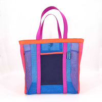 The Mother | Yacht Rock—an eye-catching beach tote with pink and orange handles, blue and purple panels, a front pocket featuring BUHA GOODS (women-owned) in white text; colorful, durable mesh design.