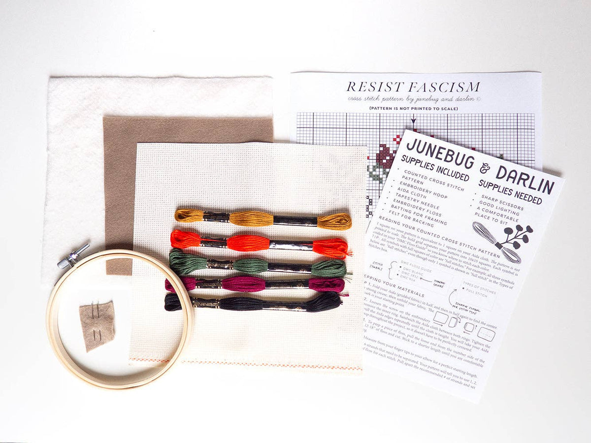The Resist Fascism Cross Stitch Kit is beginner friendly and handmade in Portland; it includes colored floss, fabric pieces, a hoop, needle, and two instruction sheets (one titled “Resist Fascism”), all arranged on a white surface.