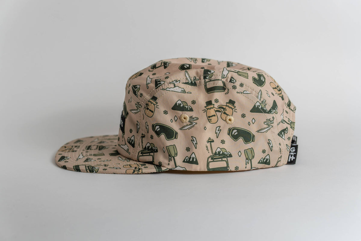 The beige First Chair 5-Panel Hat features a flat brim, water-resistant performance polyester, and playful green and yellow outdoor-themed graphics—making it the perfect cap for adventure lovers.