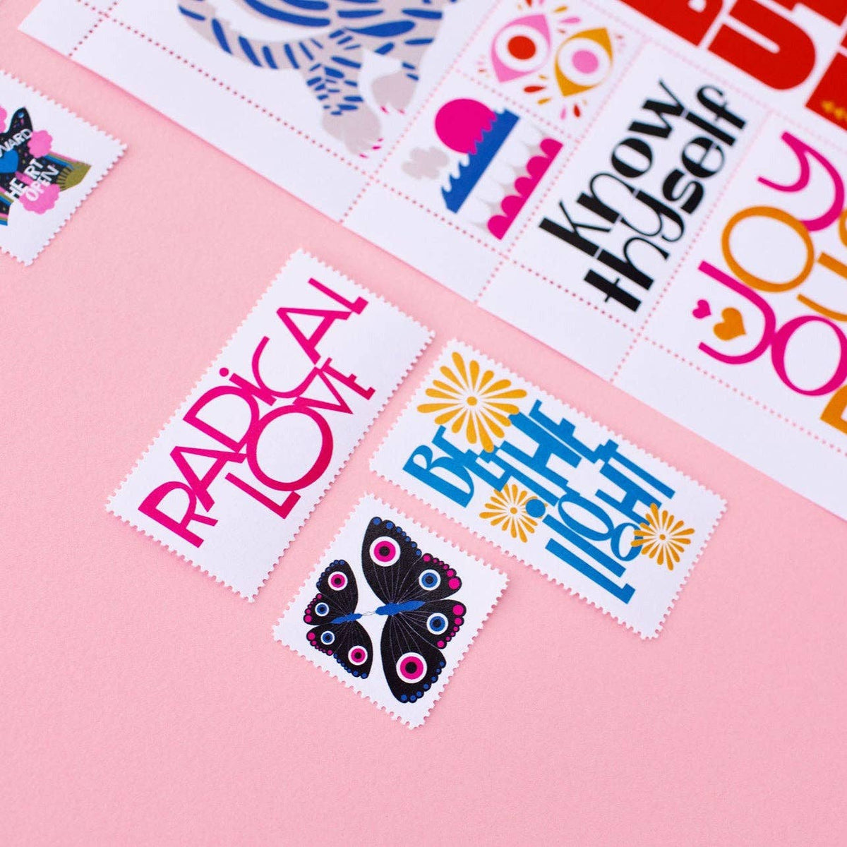 Poster Stamp Series 7 | Hold It Lightly features colorful rectangular stickers with phrases like RADICAL LOVE and Know thyself, plus floral and butterfly designs, arranged on a pink surface like unique poster stamps.