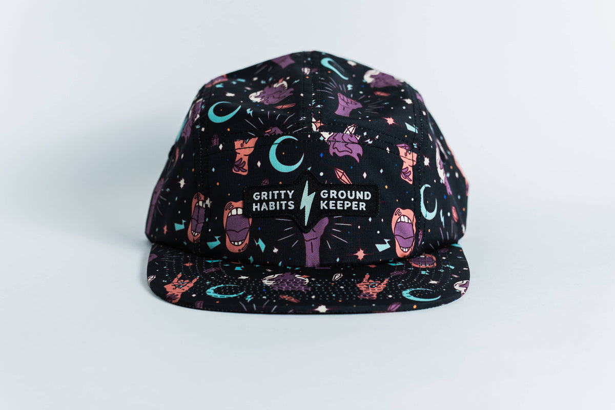 The Gritty Habits x Ground Keeper: Howl Collection 5-Panel Hat is a black snapback featuring colorful cartoon hands, mouths, stars, and moons. The front reads GRITTY HABITS ⚡ GROUND KEEPER. Proudly women-owned.