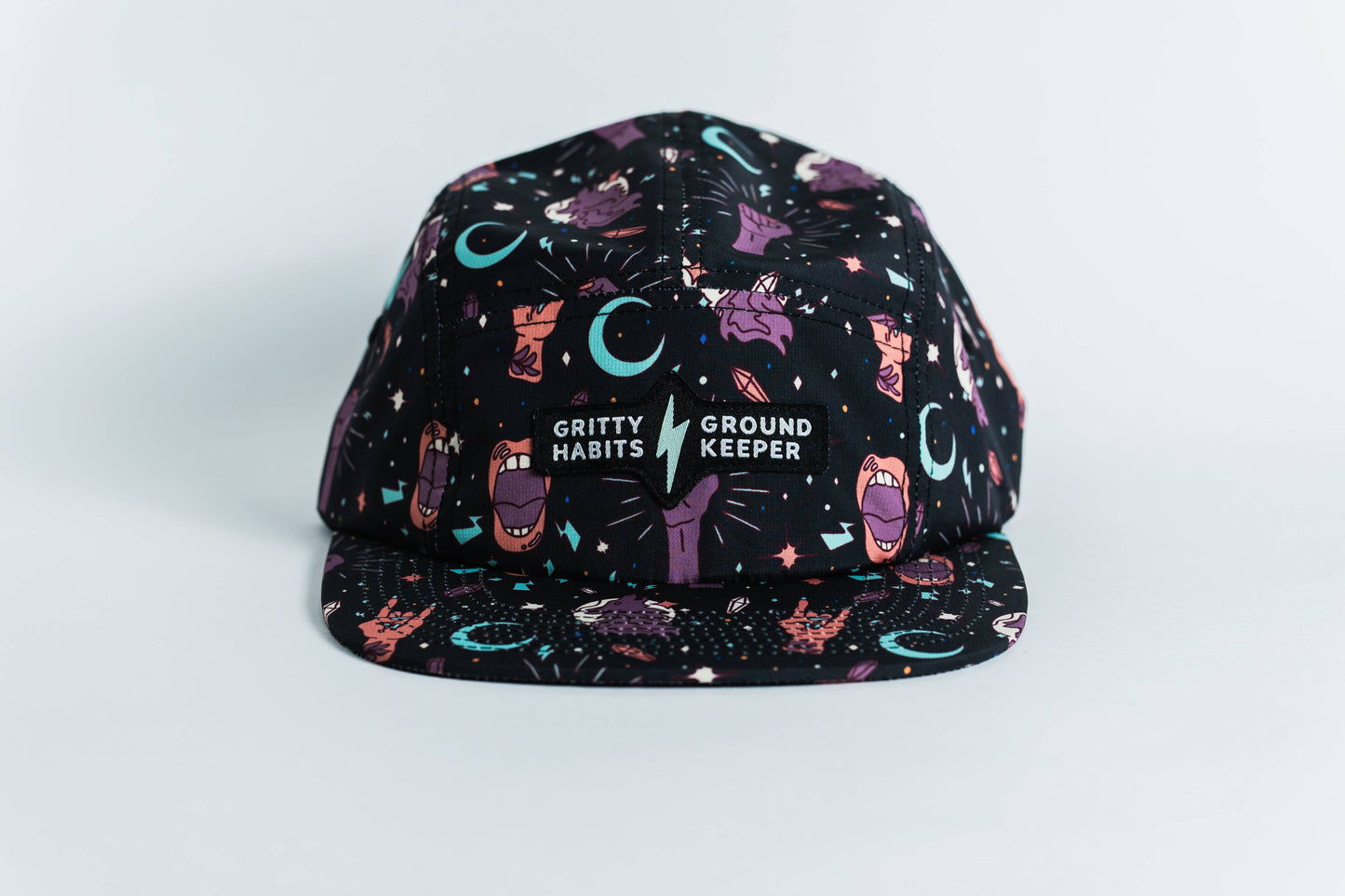 The Gritty Habits x Ground Keeper: Howl Collection 5-Panel Hat is a black snapback featuring colorful cartoon hands, mouths, stars, and moons. The front reads GRITTY HABITS ⚡ GROUND KEEPER. Proudly women-owned.