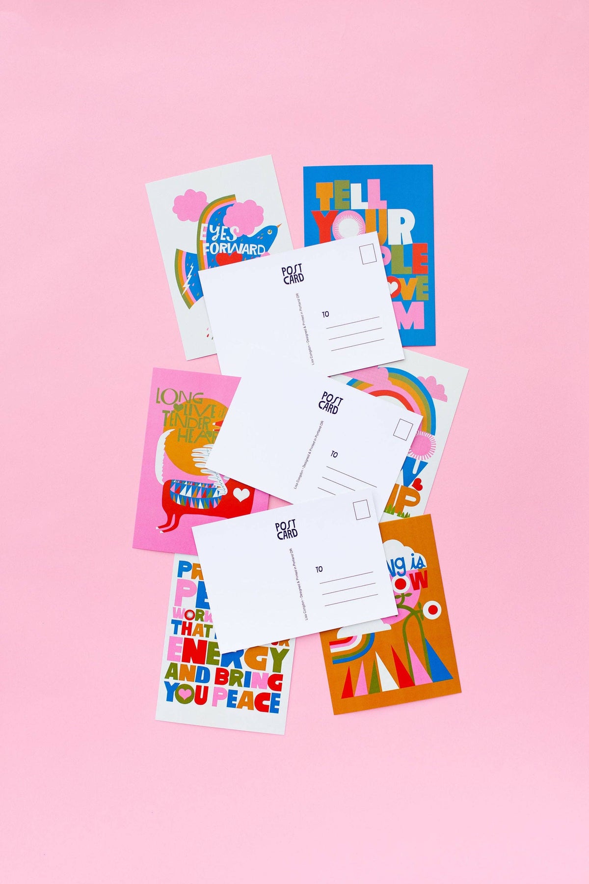 The XL Postcard Set features colorful, bold postcards with encouraging messages, displayed on a pink background to show both the vibrant fronts and standard white backs. Every postcard is proudly printed in Portland.
