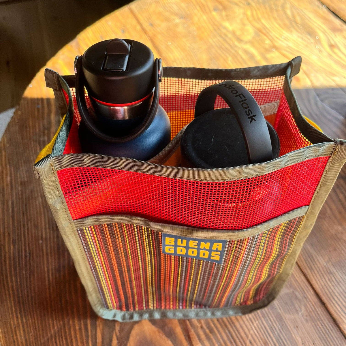 The Two-Bottle-Bag | Cava on the Playa holds two water bottles, including a Hydro Flask, and features striped fabric with mesh sides—ideal for outings and shown here on a wooden table.