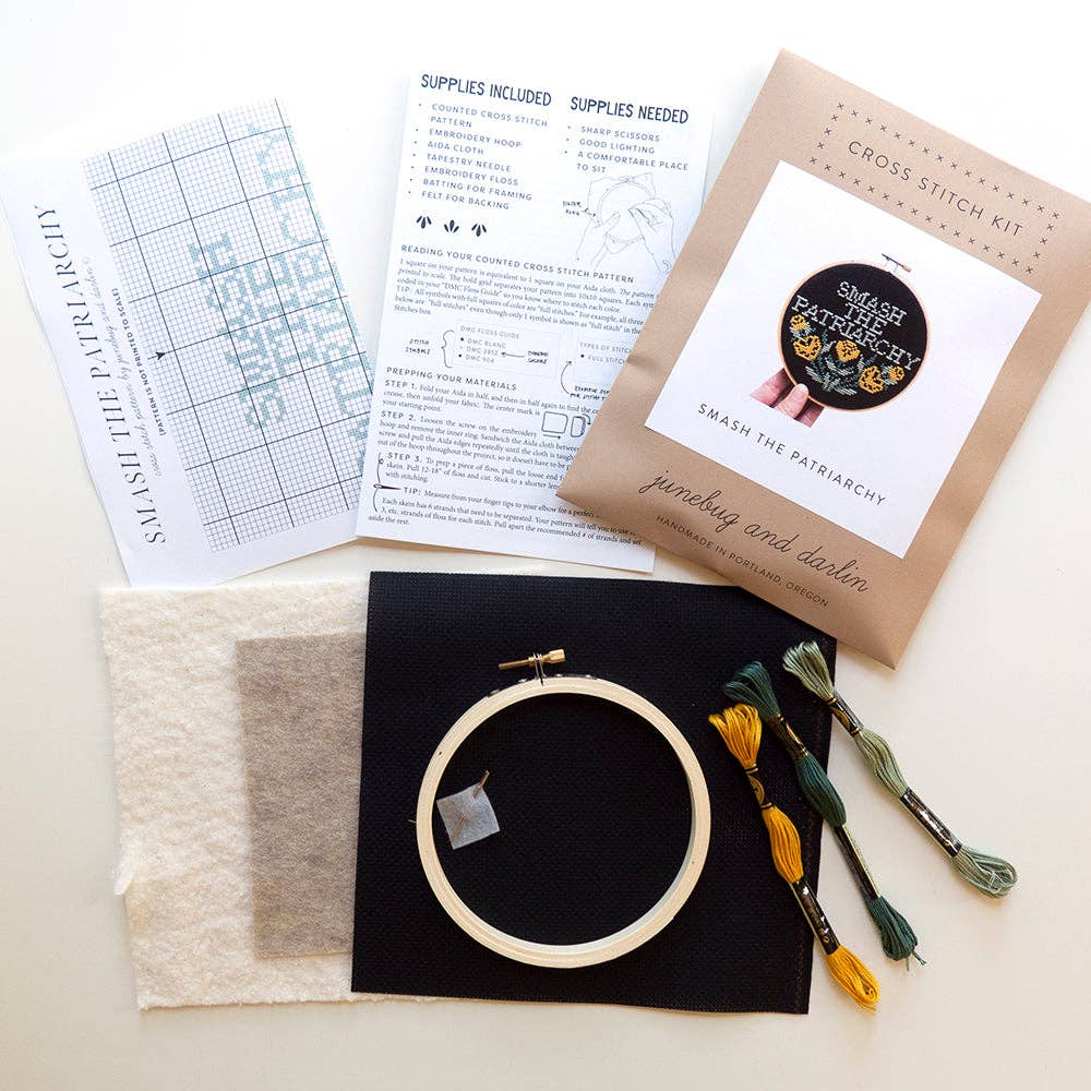 The Smash the Patriarchy Cross Stitch Kit is beginner-friendly and includes a chart, instructions, black fabric, white felt, colorful floss, a wooden hoop, needle, and bold "Smash the Patriarchy" packaging.