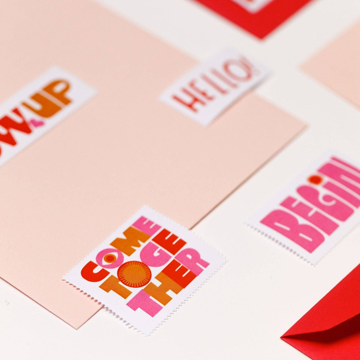 Poster Stamp Series 5 | Words to Live By features colorful stickers inspired by Lisa Congdon, with positive words like “COME TOGETHER” and “BEGIN,” arranged cheerfully on pale pink and white with a red envelope.