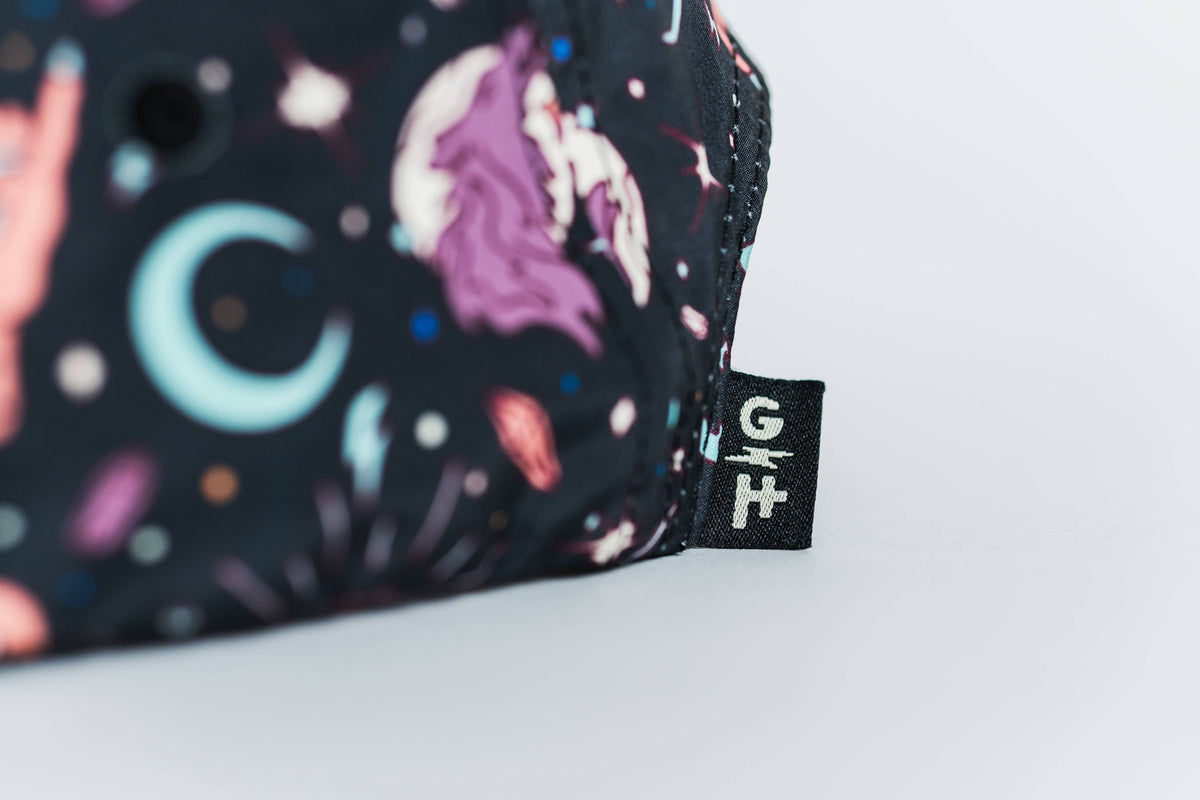 Close-up of the Gritty Habits x Ground Keeper: Howl Collection 5-Panel Hat—black fabric with colorful space-themed designs, crescent moon and planets, plus a small black G/H tag marks this women-owned brand's unique style.