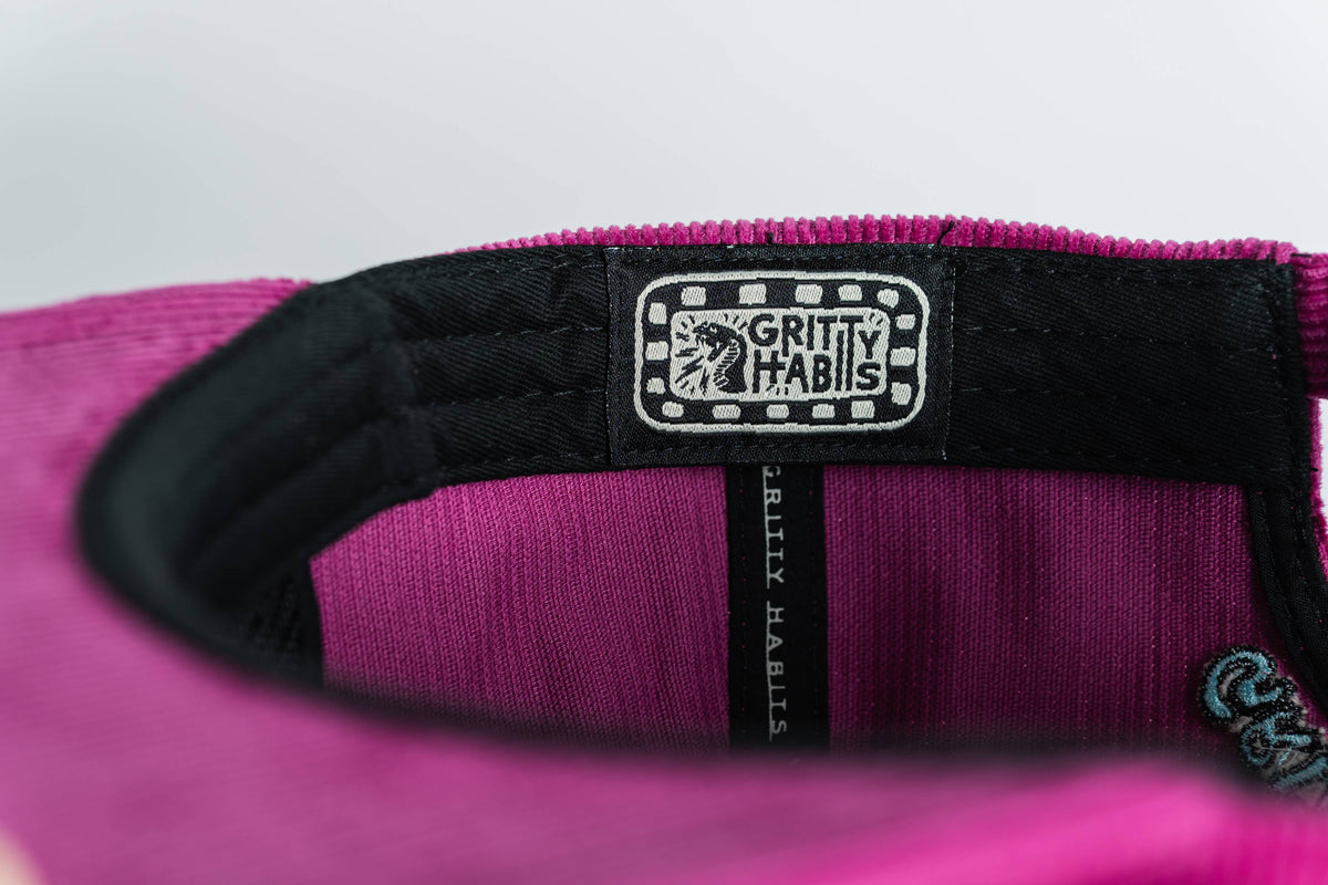 Close-up of a clothing label inside the Shred Til She's Dead Corduroy 5-Panel Hat, reading GRITTY HABITS with a decorative border and small emblem—spotlighting this women-owned small business.