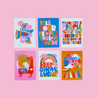 The XL Postcard Set features six colorful postcards with bold, vibrant text and playful illustrations on a pink background, offering encouraging messages of positivity, love, and peace. Proudly printed in Portland to inspire you every day.