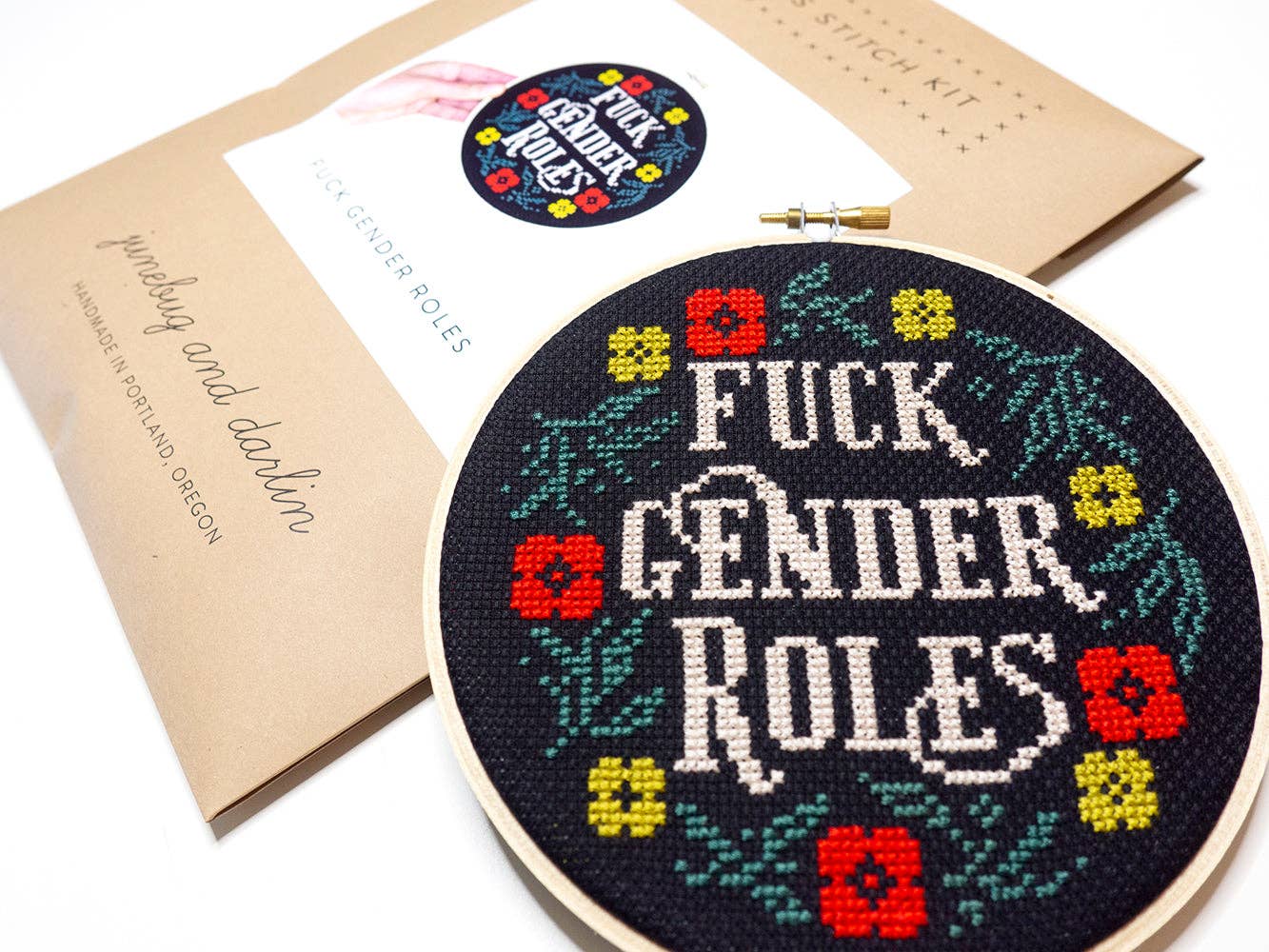 The Fuck Gender Roles Cross Stitch Kit features a round hoop with “Fuck Gender Roles” stitched in white on black fabric, surrounded by colorful flowers. This handmade, beginner-friendly kit includes matching cross-stitch instructions.