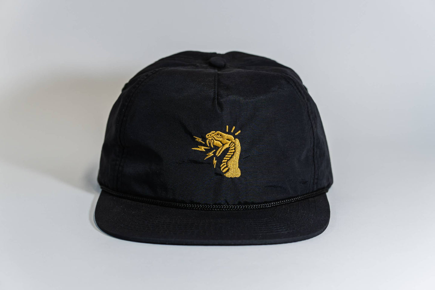 The Fearless 5-Panel Hat is a black cap with an embroidered yellow cobra, mouth open and tongue out, on the front. Displayed on a white background, it's part of the Gritty Habits collection.