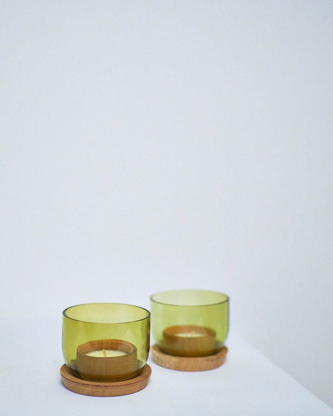 Two Taa Tea Lights Candle Holders, crafted from upcycled green wine bottles with wooden bases for tealights, are displayed side by side on a white surface against a plain light background.