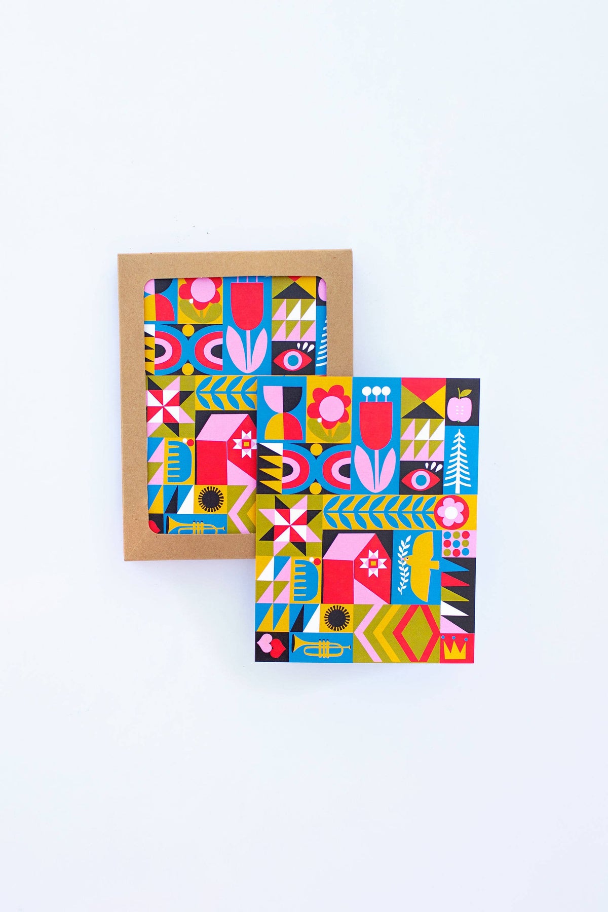 Two Blank Quilt Squares Greeting Cards featuring bold geometric and floral patterns in red, blue, yellow, and black; one card is boxed in brown kraft paper and the other is outside, both displayed on a white background.
