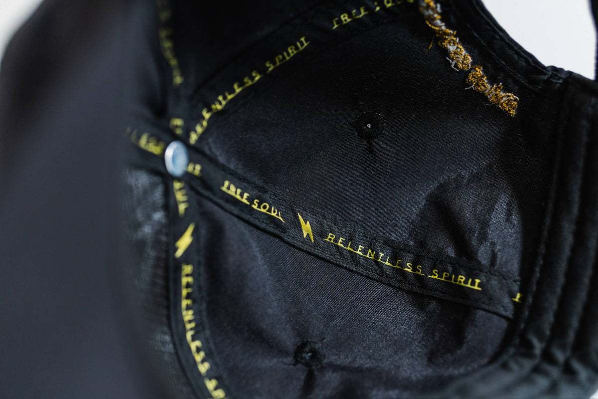 Close-up of black fabric on the Fearless 5-Panel Hat, featuring stitched yellow text "RELENTLESS SPIRIT" and "FREE SOUL" with a lightning bolt symbol, suggesting Gritty Habits style.