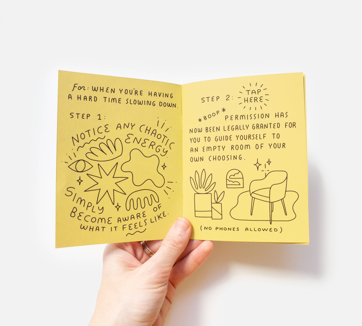 A hand holds open the Take a Break Zine, an eco-friendly, handmade booklet featuring hand-drawn doodles and steps to slow down—like noticing chaos and granting yourself permission to rest—with charming illustrations of plants and a chair.