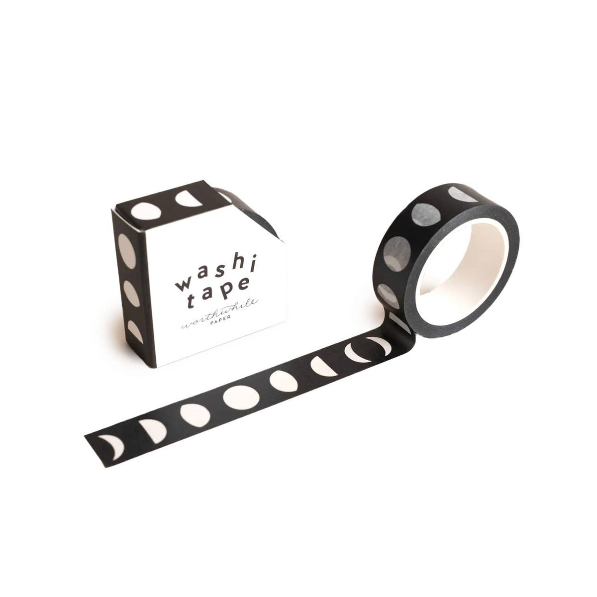 The Moons Washi Tape, an eco-friendly black tape featuring a striking white lunar phases pattern, is partially unrolled beside its matching "washi tape" box for a stylish and sustainable display.