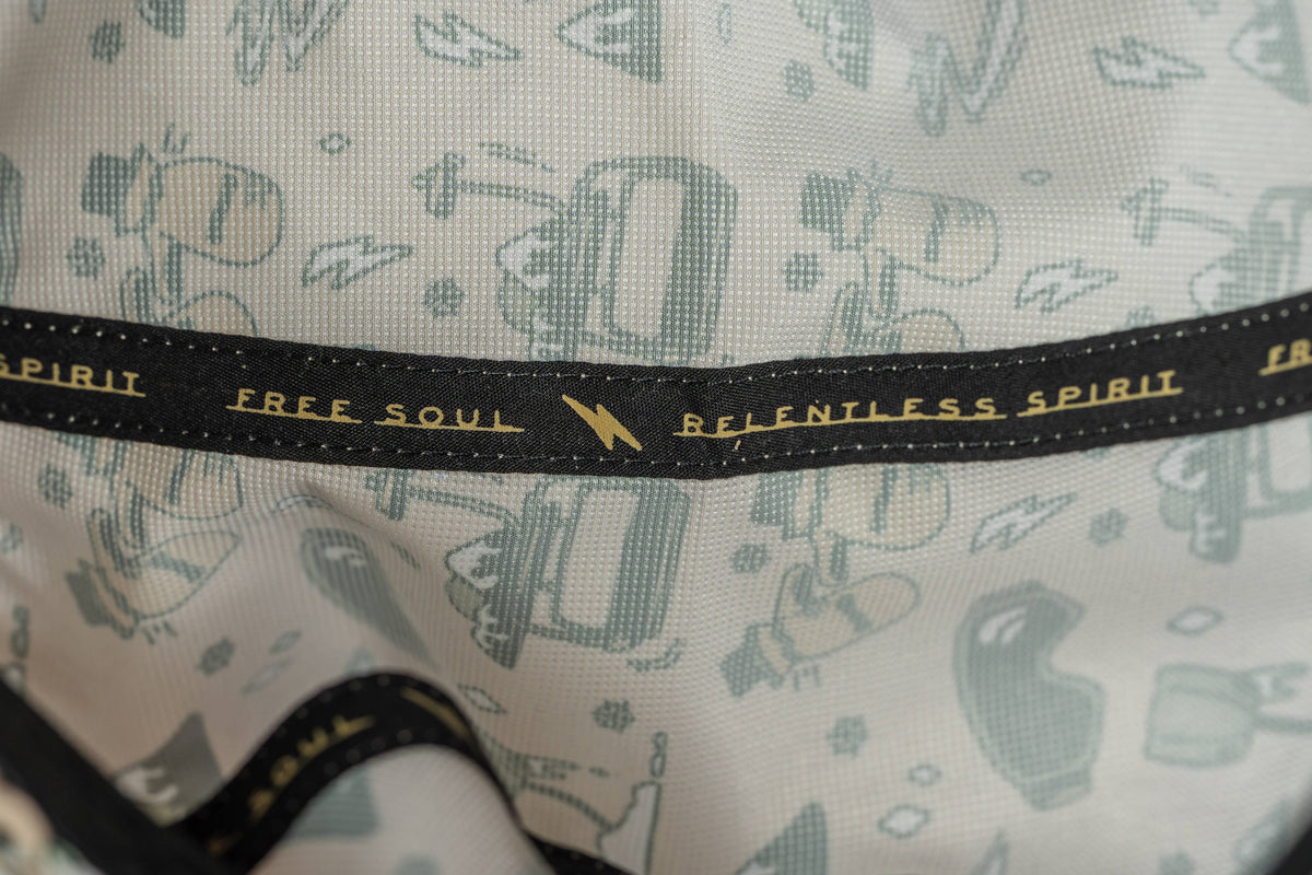 A close-up of the First Chair 5-Panel Hat’s performance polyester fabric in light blue with small object patterns and a black band reading FREE SOUL and RELENTLESS SPIRIT in gold—a water-resistant hat detail.