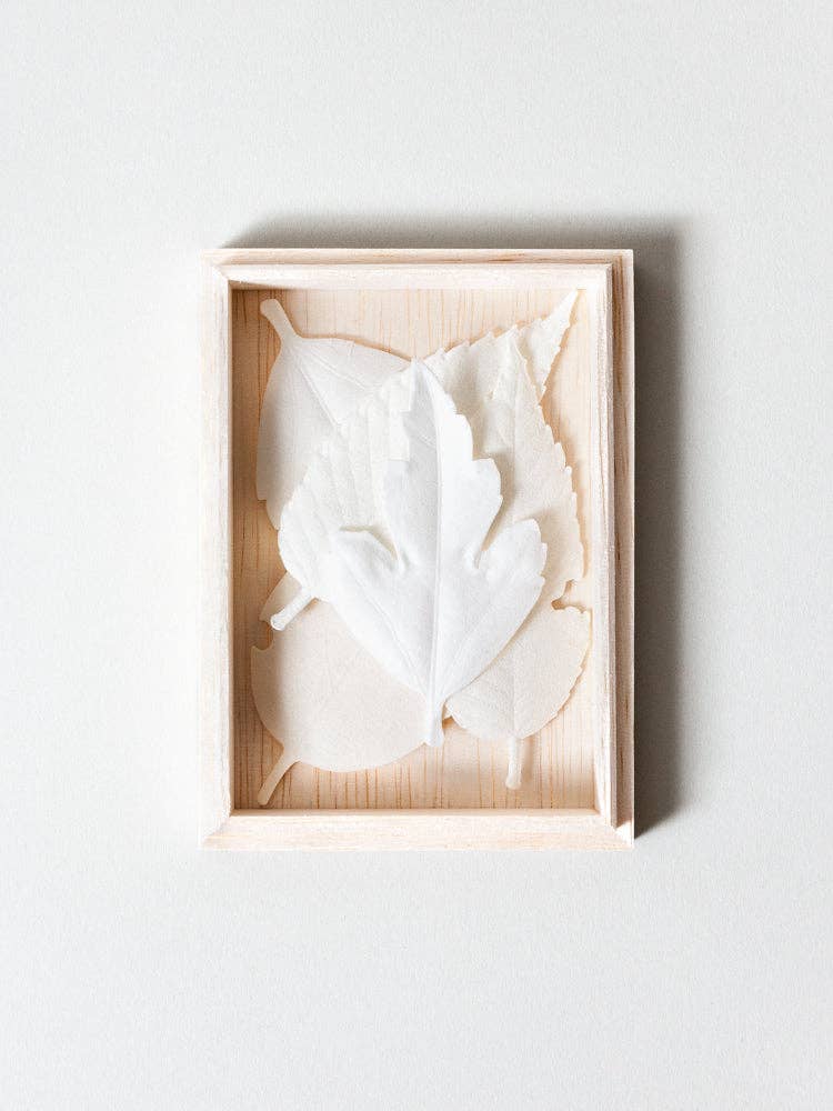 A small, light wooden frame displays three overlapping translucent white leaves—mirroring the minimalistic elegance of HA KO Paper Incense—against a plain white background for a delicate, serene effect.