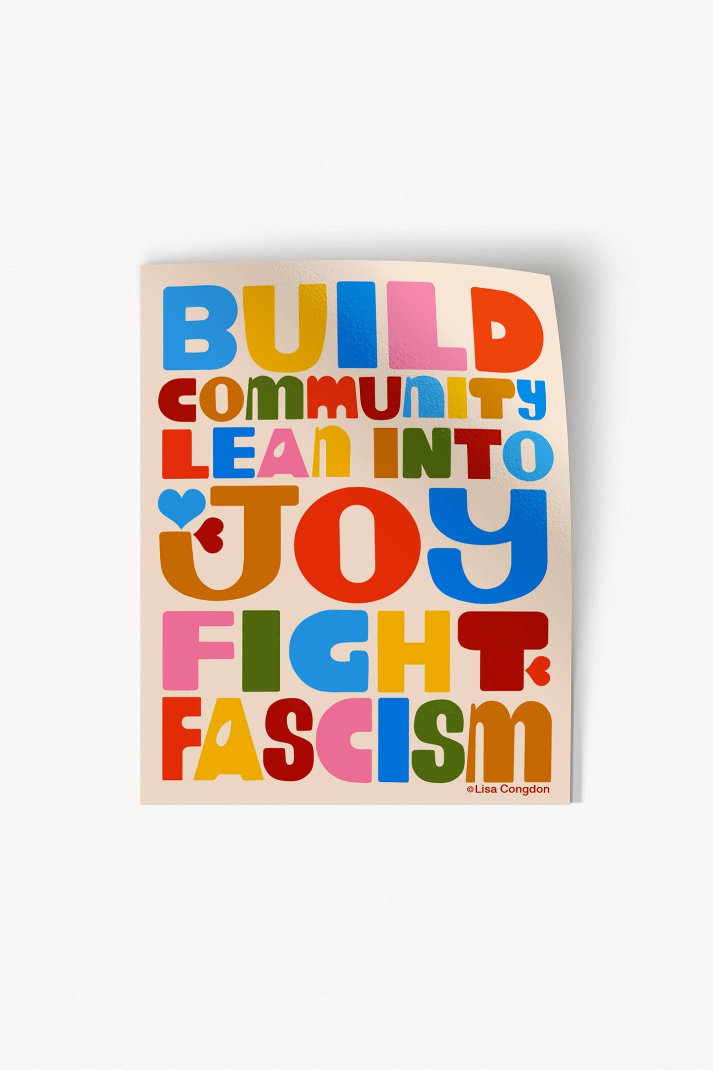 Build Community Large Sticker: XL waterproof sticker with bold, colorful letters—BUILD COMMUNITY LEAN INTO JOY FIGHT FASCISM—on white. Lisa Congdon-inspired playful fonts, heart detail in JOY. Perfect for personalizing your space!.