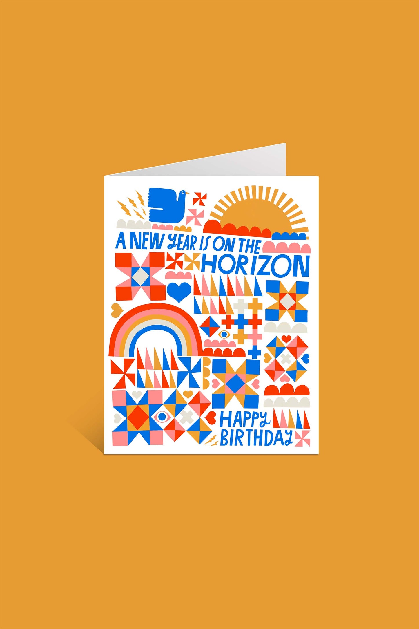 The "A New Year is on the Horizon Greeting Card" showcases Lisa Congdon's vibrant art with bold patterns, hearts, a rainbow, and sun. “A NEW YEAR IS ON THE HORIZON” and “HAPPY BIRTHDAY!” in blue and orange on FSC-certified paper.