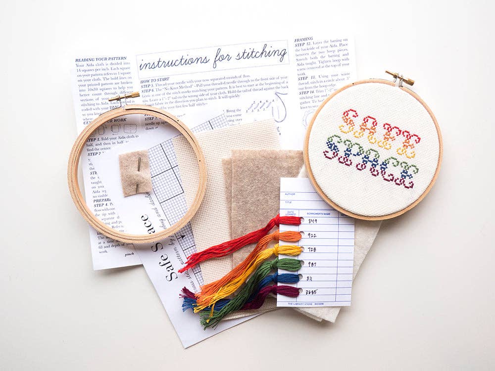 The Safe Space Cross Stitch Kit is beginner-friendly and includes instructions, colored threads, fabric pieces, and two hoops—one featuring “SAFE SPACE” stitched in rainbow colors. Great for handmade creations.