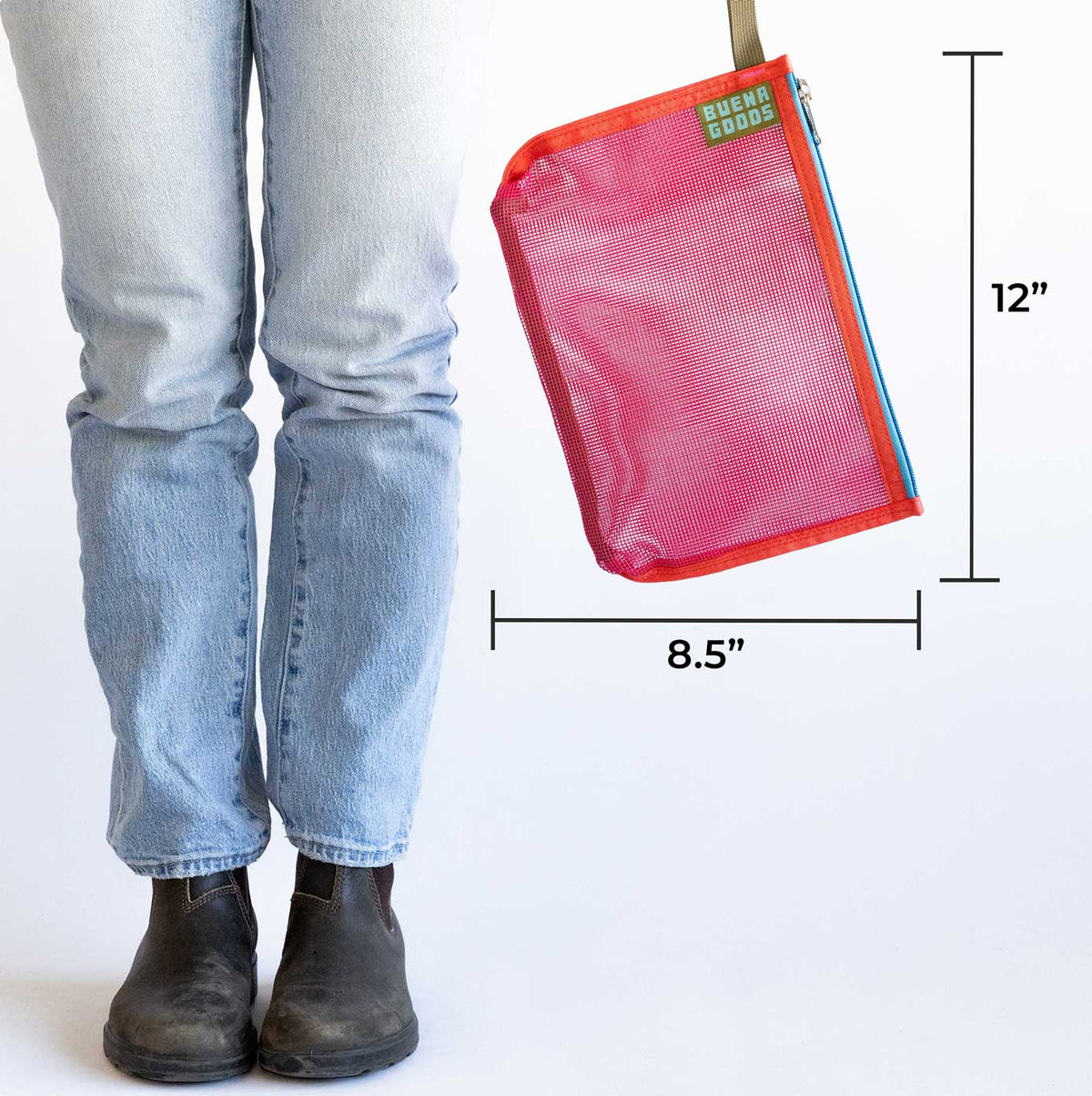 A person in light blue jeans and black boots stands beside The Keeper | Yacht Rock—a red industrial mesh zippered pouch (12" x 8.5") with a measurement line for scale—featuring a “Buenas Goods” label and versatile organizer design.