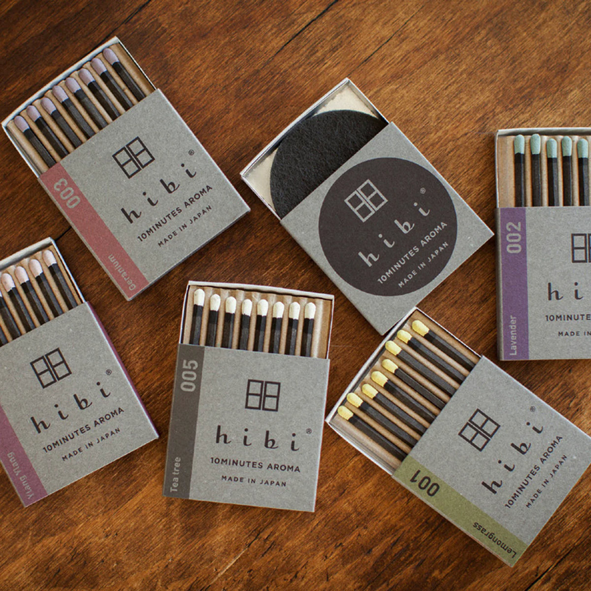 Five boxes of Hibi Japanese Incense Matches in assorted scents are arranged on wood, one open to display the matches and circular burning pad. Perfect travel incense for relaxation wherever you go.