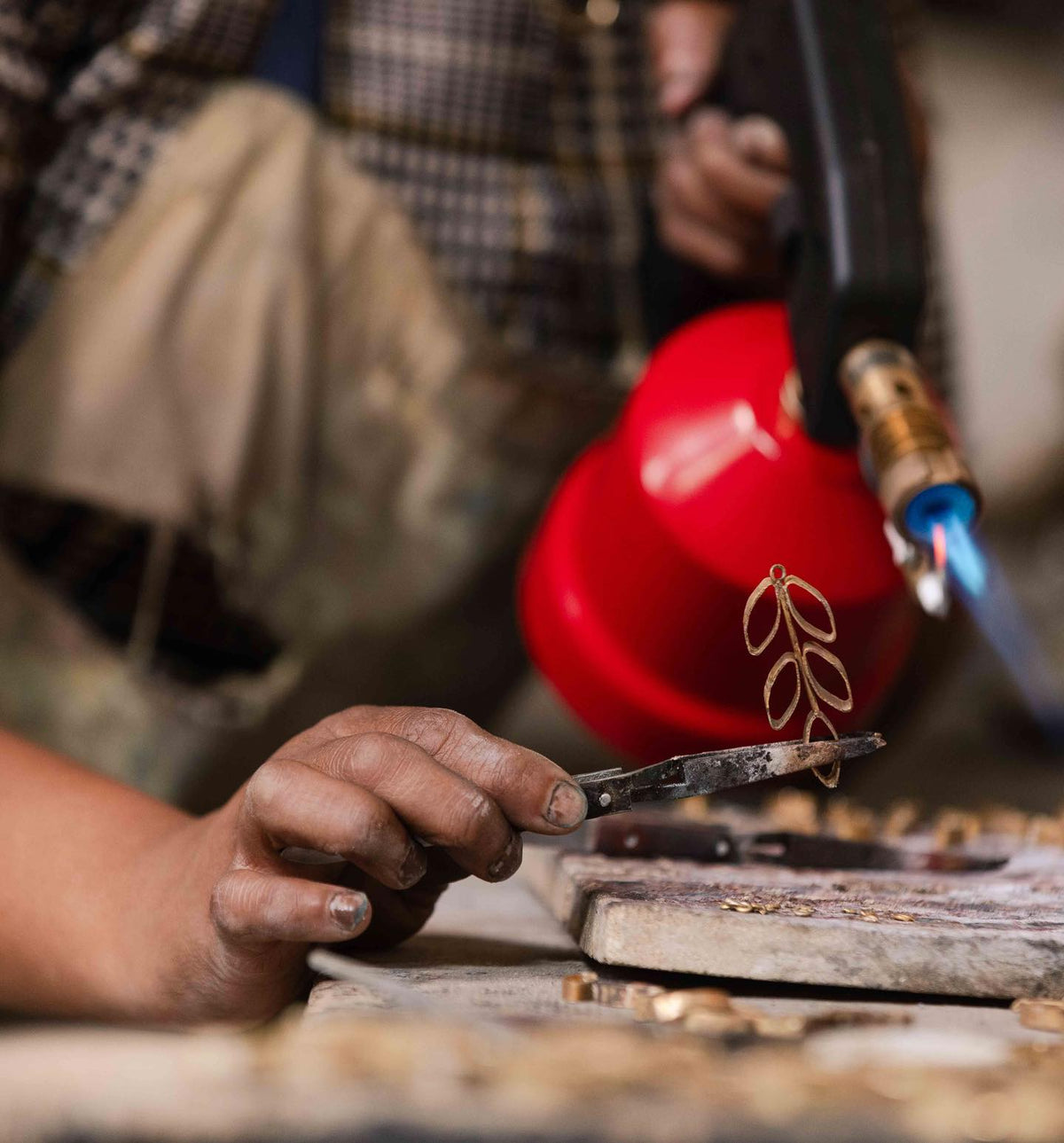 A person uses a blowtorch and tweezers at a workbench to craft Posy Paper Pulp Earrings, carefully shaping the delicate accessory.